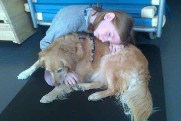 Tiergestützte Arbeit Ausbildung - junge Frau umarmt liegenden Golden Retriever