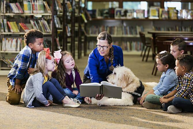 therapiebegleithunde trainer ausbildung kinder in einer bibliothek lesen gemeinsam mit einem therapiebegleithund ein buch